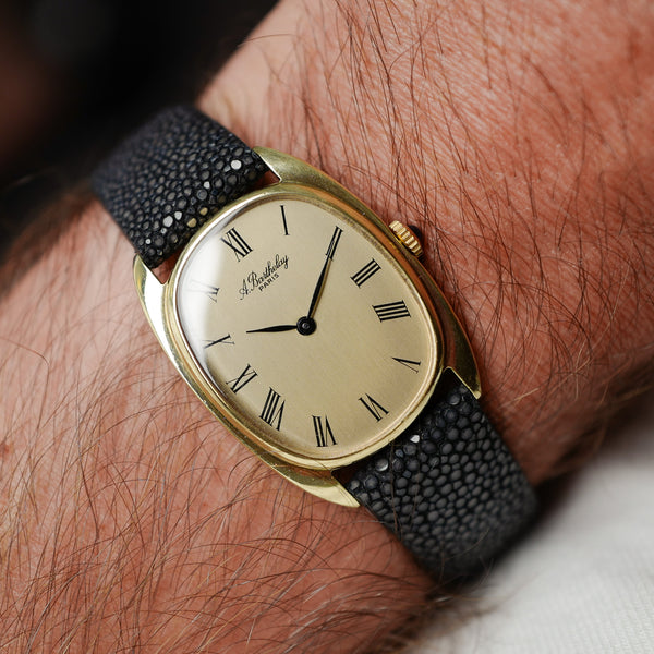 Boîtier elliptique plaqué or et bracelet noir au poignet